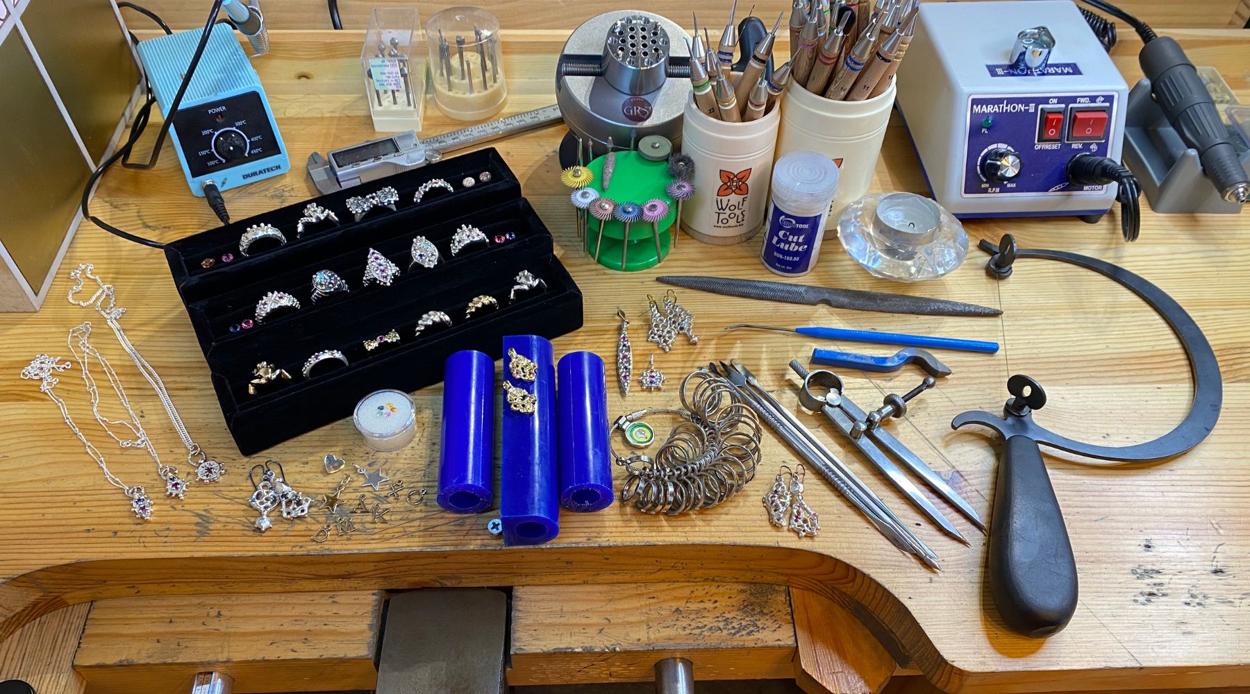 Madame Mak Jewellery Workbench in Melbourne, Australia. The image showcases a well-organized work area with a wooden jewelry bench placed against a wall. The bench is equipped with various tools and materials for jewelry making, including pliers, hammers, and  Madame Mak Jewellery
